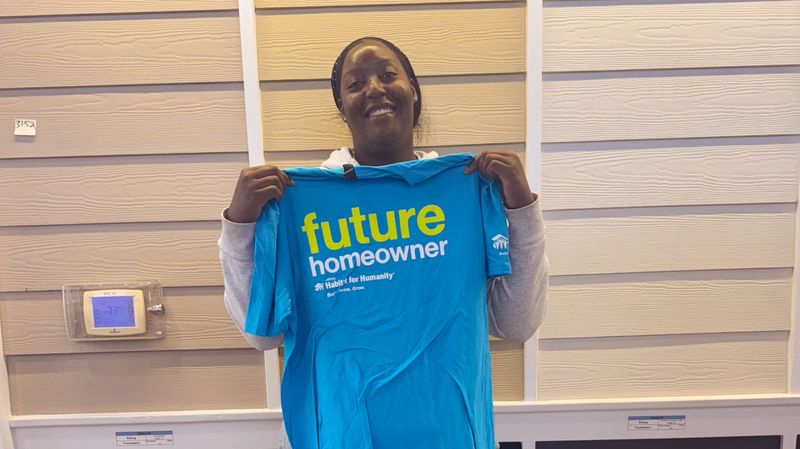 Charday Clark, a future Langston Park homeowner, holding up a Future Homeowner t-shirt and smiling